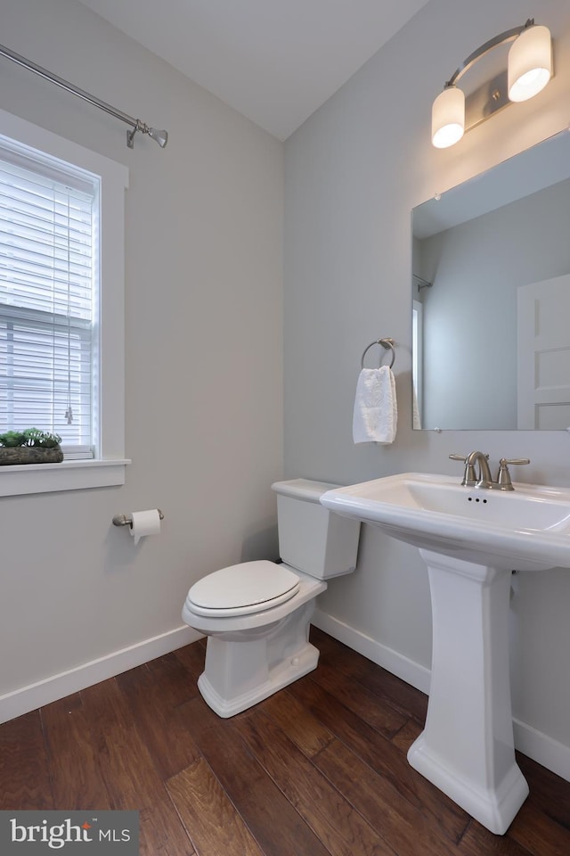 half bathroom with toilet, baseboards, and wood finished floors