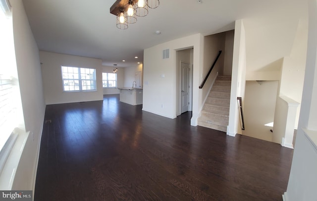 unfurnished living room featuring dark wood finished floors, visible vents, a notable chandelier, and stairs