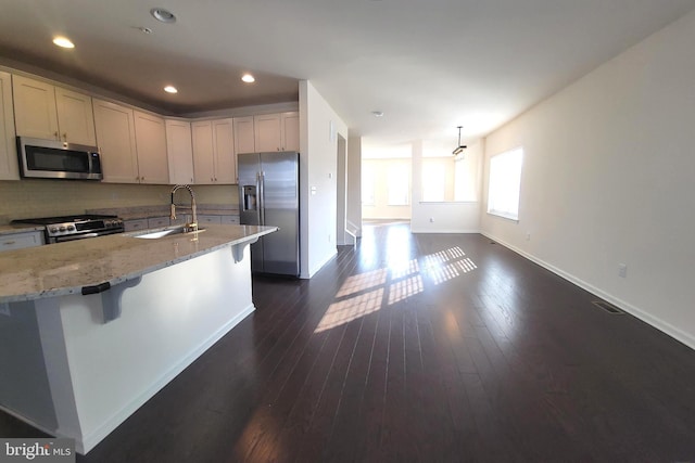 kitchen with baseboards, light stone counters, dark wood-type flooring, stainless steel appliances, and a sink