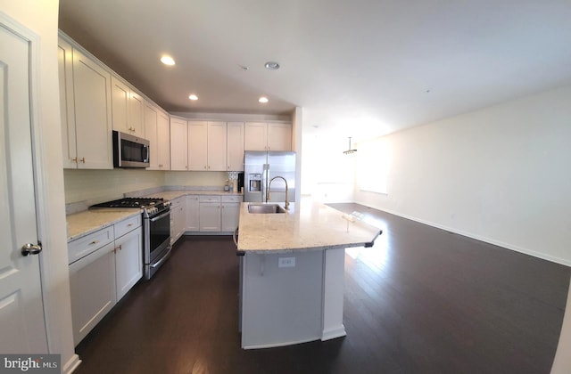 kitchen featuring light stone counters, dark wood-style flooring, a sink, appliances with stainless steel finishes, and backsplash