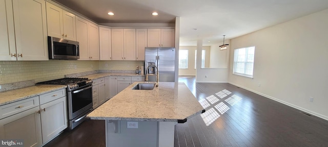 kitchen featuring stainless steel appliances, backsplash, a sink, light stone countertops, and baseboards