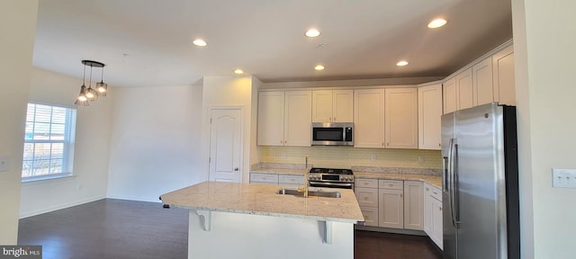 kitchen featuring dark wood finished floors, stainless steel appliances, tasteful backsplash, a sink, and light stone countertops