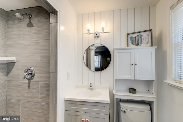 bathroom with toilet, a tile shower, and vanity