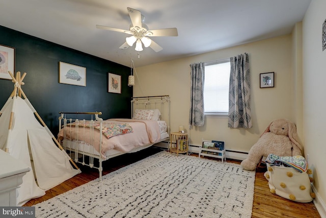 bedroom with ceiling fan, an accent wall, wood finished floors, and baseboards