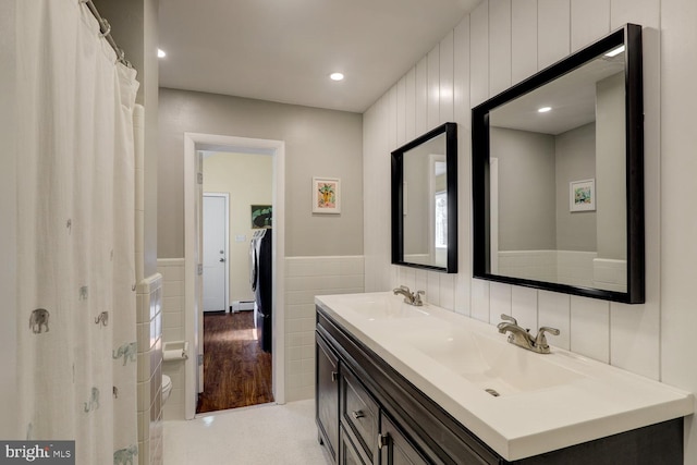 full bathroom with double vanity, tile walls, a sink, and wainscoting