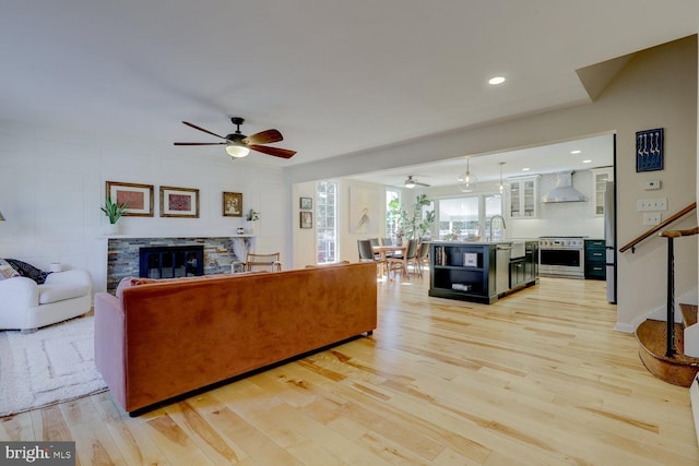 living room featuring light wood finished floors, recessed lighting, a ceiling fan, a stone fireplace, and stairs