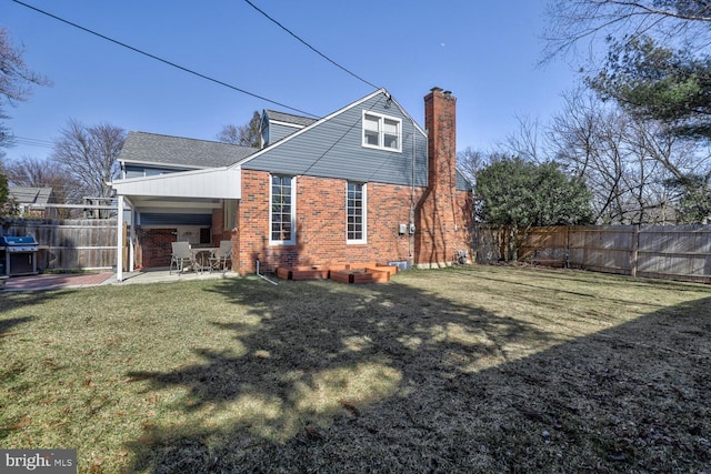 back of house featuring a fenced backyard, brick siding, a lawn, a chimney, and a patio area