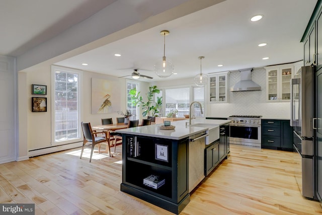 kitchen featuring stainless steel appliances, light wood-style flooring, a baseboard heating unit, a sink, and wall chimney exhaust hood