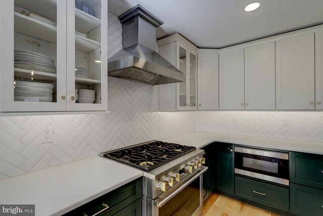 kitchen with light countertops, green cabinets, appliances with stainless steel finishes, white cabinetry, and wall chimney exhaust hood