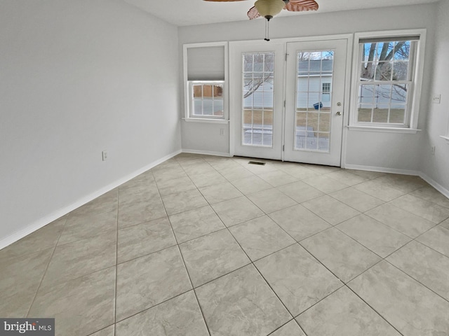 tiled spare room with visible vents, a ceiling fan, and baseboards