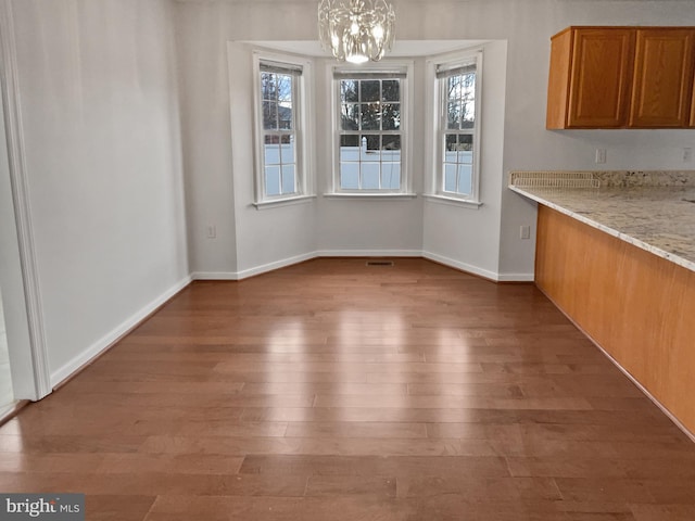 unfurnished dining area featuring baseboards, visible vents, a chandelier, and wood finished floors