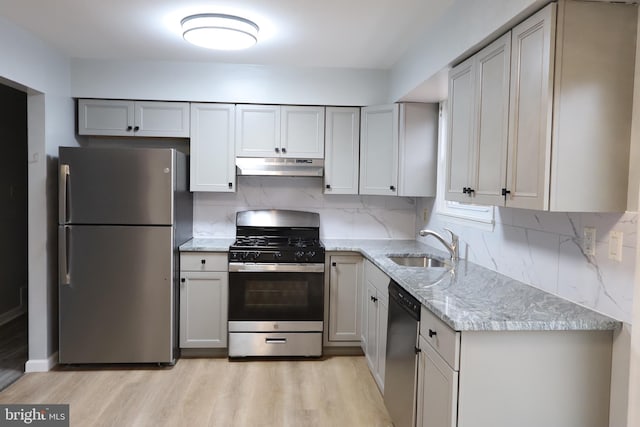 kitchen featuring stainless steel appliances, a sink, under cabinet range hood, and light stone counters