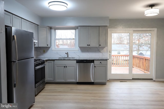 kitchen featuring stainless steel appliances, a sink, decorative backsplash, and light stone counters