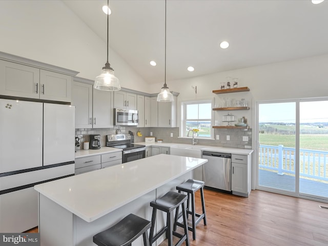 kitchen featuring backsplash, light countertops, a kitchen bar, gray cabinets, and appliances with stainless steel finishes