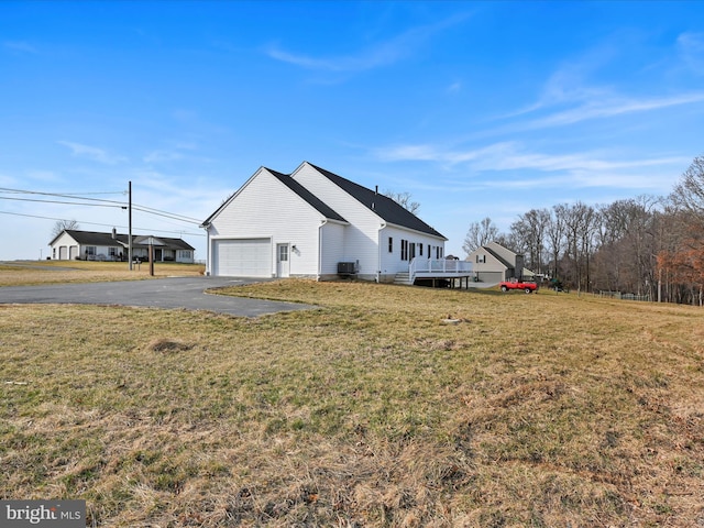 view of side of property with aphalt driveway, central air condition unit, and a yard