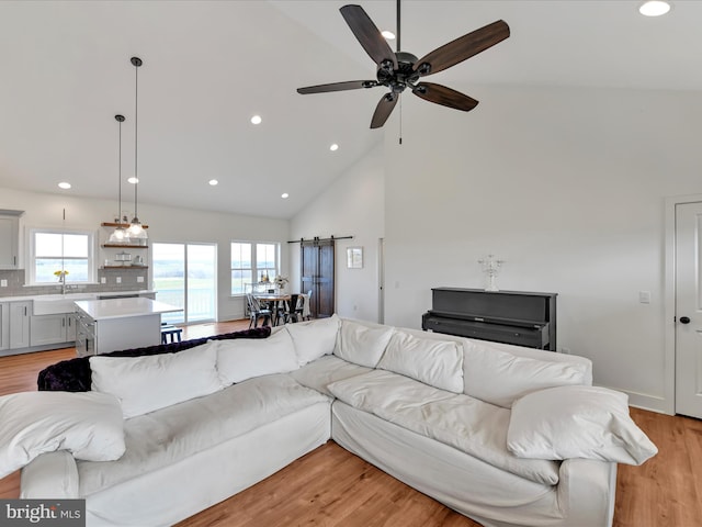 living room with high vaulted ceiling, recessed lighting, ceiling fan, light wood-style floors, and a barn door