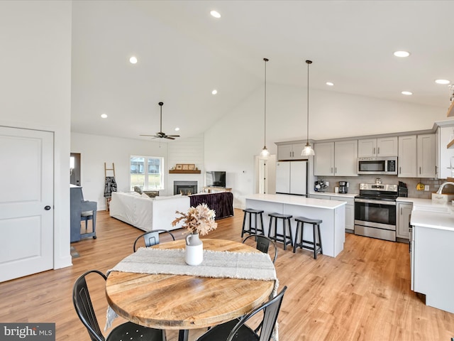 dining area featuring high vaulted ceiling, light wood-style floors, a warm lit fireplace, and a ceiling fan