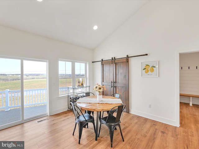 dining area with a barn door, light wood-style floors, visible vents, and baseboards