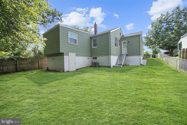 back of property with a chimney, a fenced backyard, a yard, and central AC