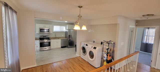 clothes washing area featuring laundry area, baseboards, light wood-style flooring, washer and dryer, and a chandelier