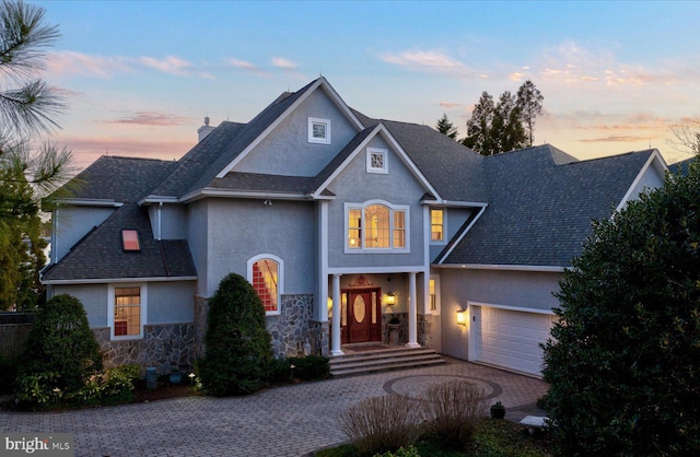 traditional home with stone siding, stucco siding, decorative driveway, and a garage