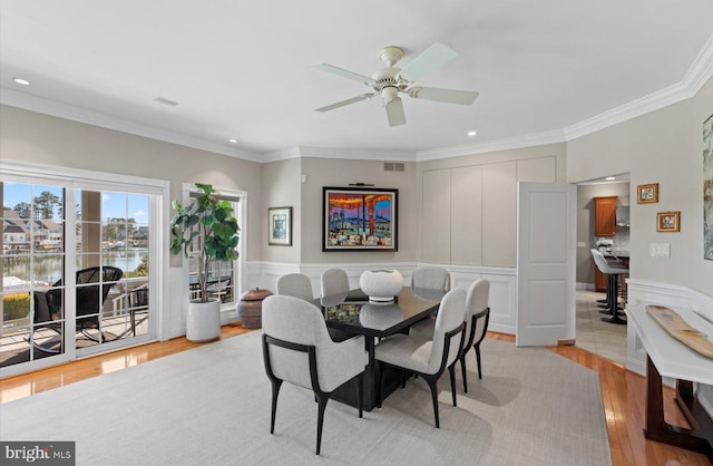 dining area with a decorative wall, light wood-style floors, and ornamental molding