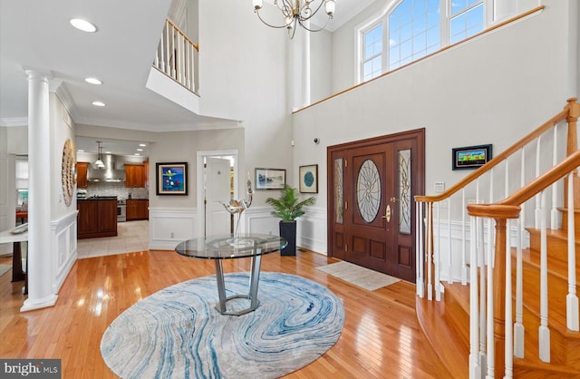 entryway featuring crown molding, light wood-style flooring, ornate columns, and wainscoting