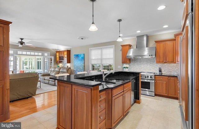 kitchen with open floor plan, brown cabinets, stainless steel appliances, wall chimney exhaust hood, and a sink