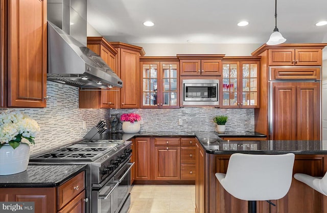 kitchen featuring a kitchen breakfast bar, built in appliances, wall chimney exhaust hood, and brown cabinetry