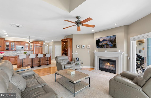 living area featuring a fireplace with flush hearth, light wood-style flooring, a ceiling fan, recessed lighting, and baseboards