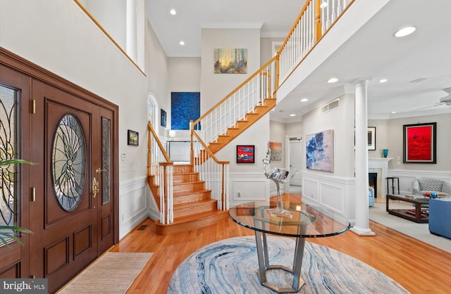 entrance foyer with visible vents, light wood-style floors, a warm lit fireplace, and ornamental molding