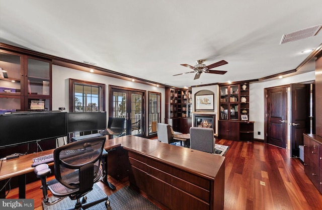 office featuring visible vents, ornamental molding, dark wood-style floors, a glass covered fireplace, and french doors