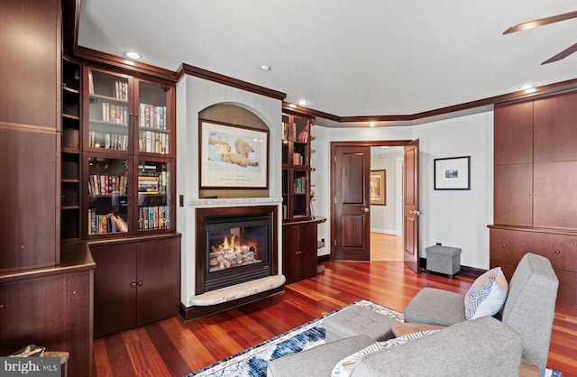 living area featuring a ceiling fan, wood finished floors, a glass covered fireplace, recessed lighting, and crown molding