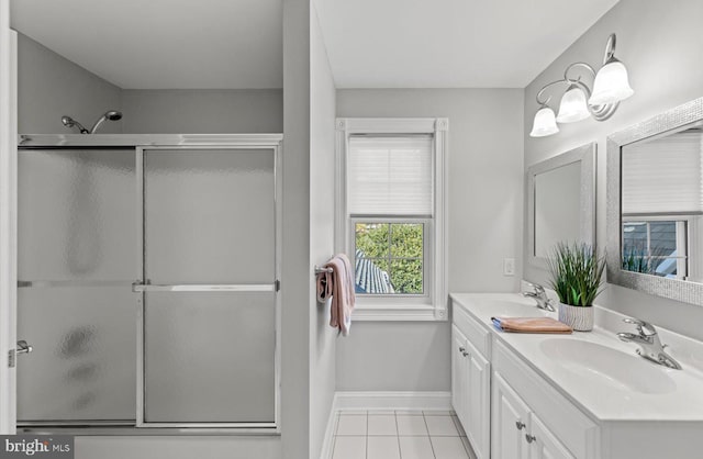 full bath with double vanity, baseboards, shower / bath combination with glass door, and a sink