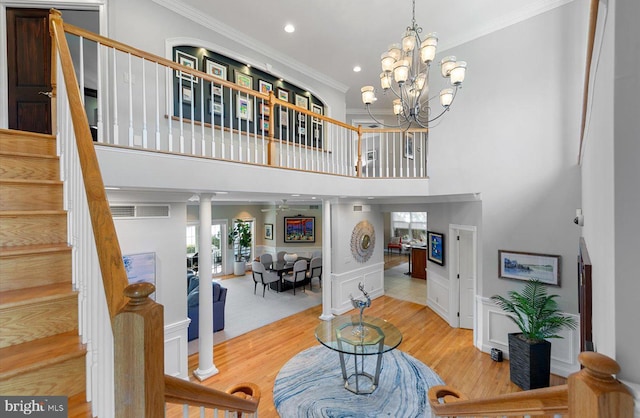 interior space with stairway, wood finished floors, an inviting chandelier, ornamental molding, and a towering ceiling