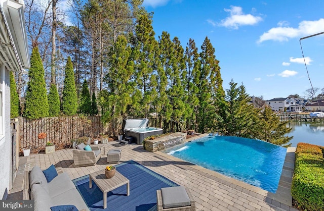 view of pool featuring a water view, fence, an outdoor hot tub, a patio area, and an infinity pool