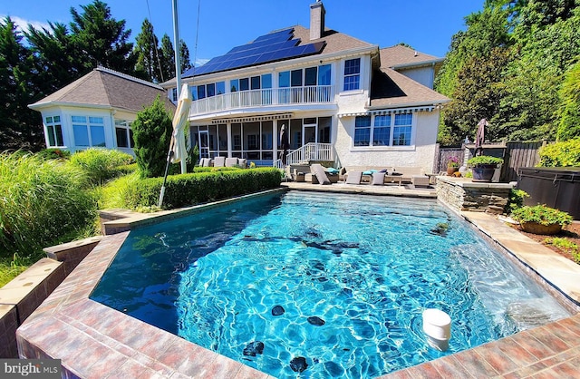 back of property featuring a balcony, a fenced in pool, a chimney, roof mounted solar panels, and an outdoor hangout area