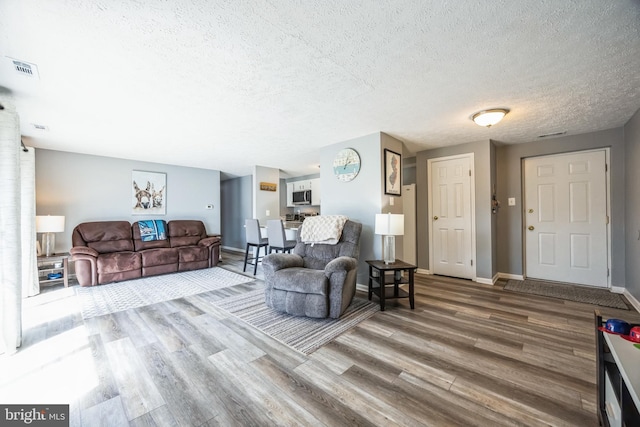 living area featuring visible vents, a textured ceiling, baseboards, and wood finished floors