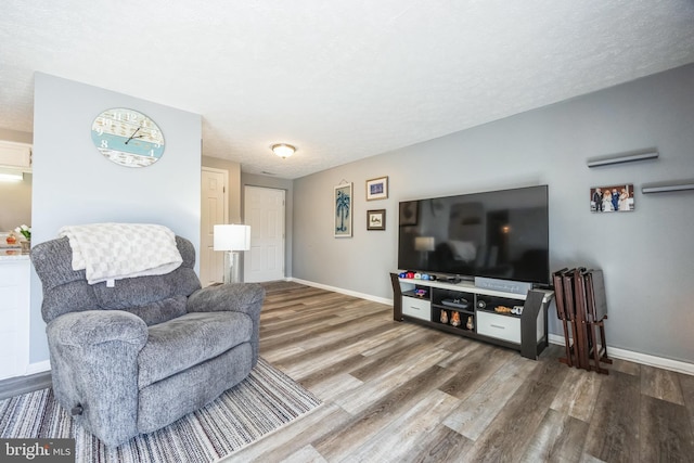 living area with baseboards, a textured ceiling, and wood finished floors