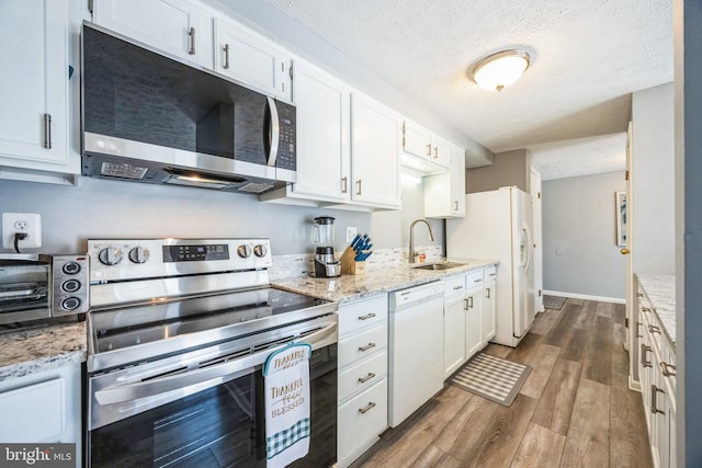 kitchen featuring a sink, white appliances, wood finished floors, and white cabinetry