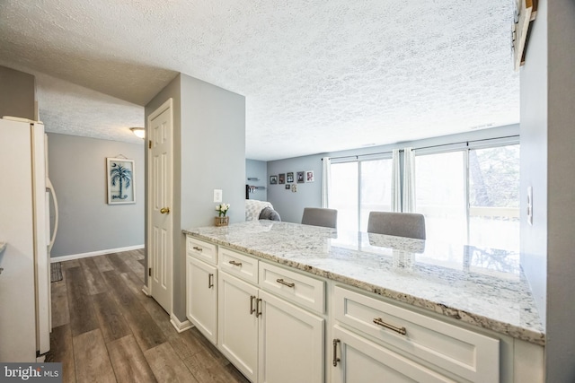 kitchen with dark wood finished floors, light stone countertops, white cabinetry, and freestanding refrigerator