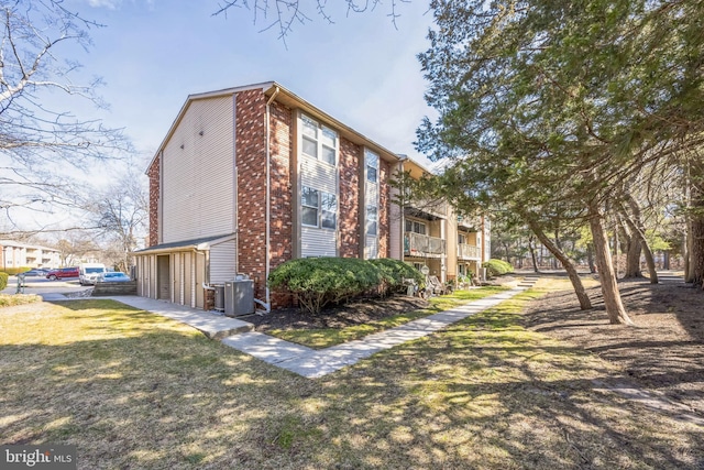 view of side of property with a garage, brick siding, central AC, and a yard