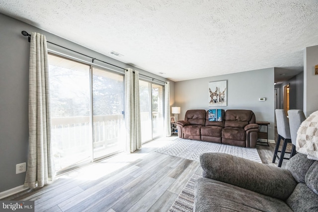 living area featuring visible vents, baseboards, a textured ceiling, and wood finished floors