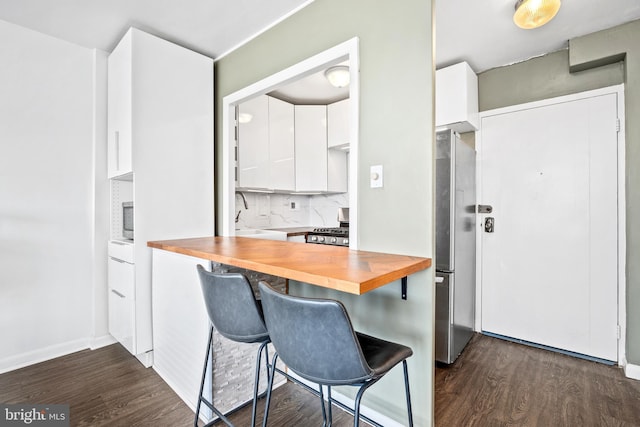 kitchen with dark wood-style floors, appliances with stainless steel finishes, white cabinets, and wooden counters