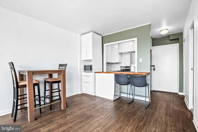 kitchen with dark wood-style floors, butcher block countertops, appliances with stainless steel finishes, white cabinetry, and a kitchen breakfast bar