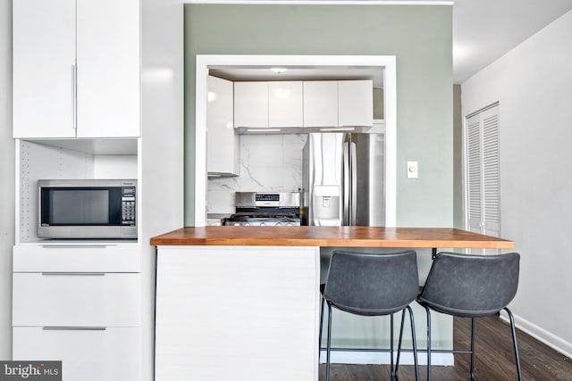 kitchen with backsplash, appliances with stainless steel finishes, white cabinets, and butcher block counters