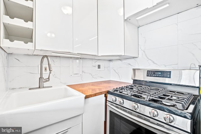 kitchen featuring backsplash, wooden counters, stainless steel gas stove, white cabinetry, and a sink