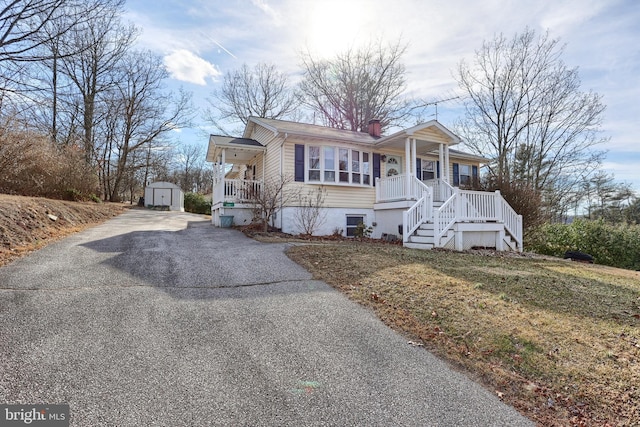 view of front of home with aphalt driveway, an outbuilding, a chimney, a storage unit, and covered porch