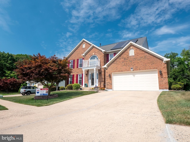 view of front of home with a balcony, brick siding, driveway, roof mounted solar panels, and a front yard