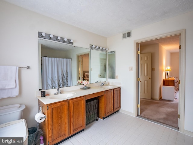 bathroom with double vanity, visible vents, toilet, a textured ceiling, and a sink